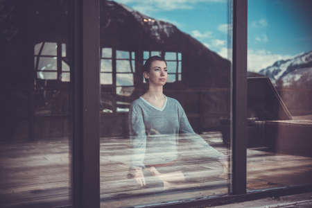 Young beautiful woman meditating while practicing yoga with mountain view in the window reflection. Freedom concept. Calmness and relax, woman happiness. Toned pictureの写真素材