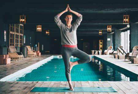 Young beautiful woman practices yoga at the swimming pool. Wellness concept. Sport and yoga, woman happiness. Toned pictureの写真素材