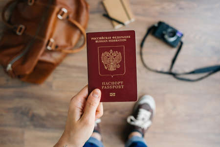 Person holds Russian travel passport in hand with leather bag and photo camera in the background. Travel and tourism concept.の写真素材