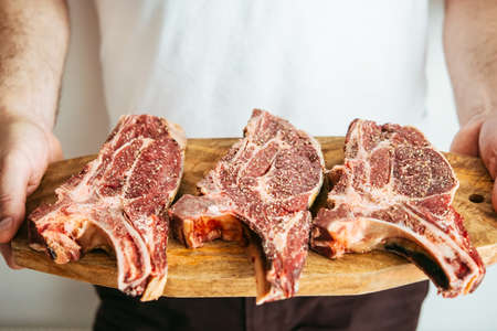 Man's hands hold three aged rib-eye beef meat steaks on wooden board