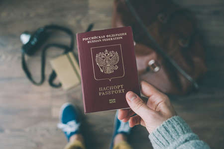 Person holds Russian travel passport in hand with leather bag and photo camera in the background. Travel and tourism concept.の写真素材