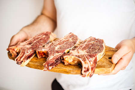Man's hands hold three aged rib-eye beef meat steaks on wooden boardの写真素材