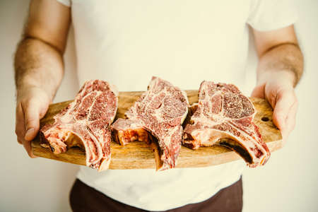 Man's hands hold three aged rib-eye beef meat steaks on wooden board. Toned imageの写真素材