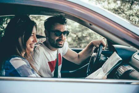 Young man and woman hold road map in a car. Travel and adventure concept. Toned pictureの写真素材
