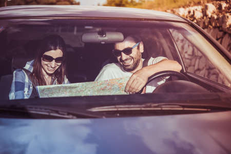 Young man and woman hold road map in a car. Travel and adventure concept. Toned pictureの写真素材