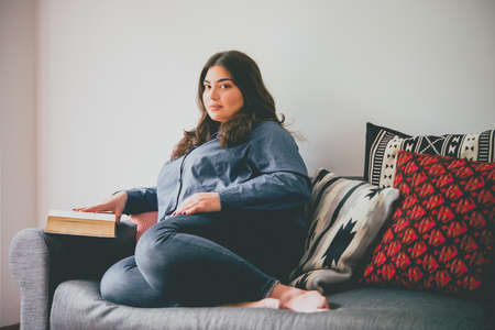 Beautiful plus size girl sitting on sofa reading a book. Toned pictureの写真素材