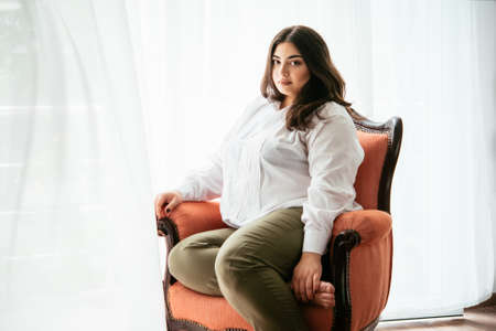 Portrait of beautiful plus size girl in white sitting in the armchairの写真素材