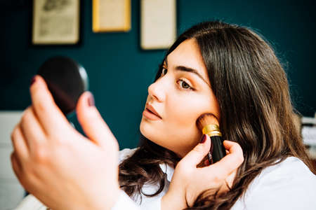 Young beautiful woman applying her make-up, looking in a mirrorの写真素材