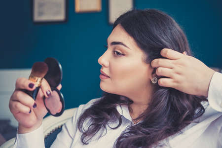 Young beautiful woman applying her make-up, looking in a mirror. Toned pictureの写真素材