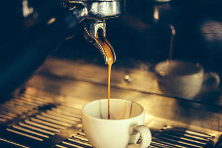 Coffee made in professional espresso machine pouring into a cup. Toned pictureの写真素材