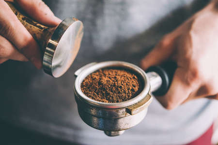 Barista presses ground coffee using tamper. Toned picture