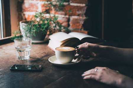 Young woman having a cup of coffee and reading a book in a cafe. Toned pictureの写真素材
