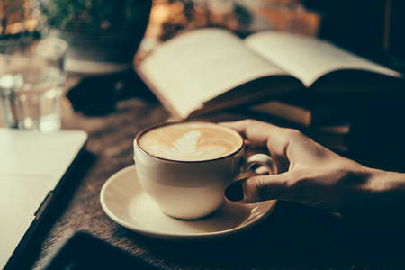 Young woman having a cup of coffee and reading a book in a cafe. Toned pictureの写真素材