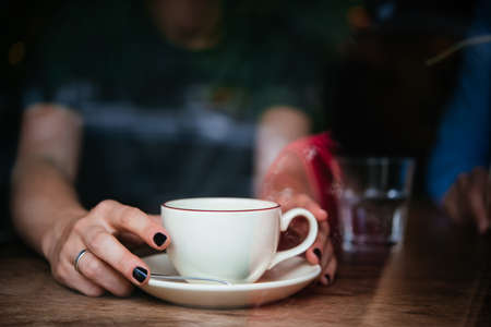 Hands of young woman holding a cup of coffee seen through cafe windowの写真素材