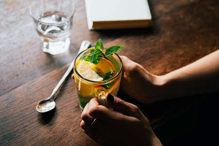 Hands of young woman holding a cup of hot mint tea or hot lemonadeの写真素材
