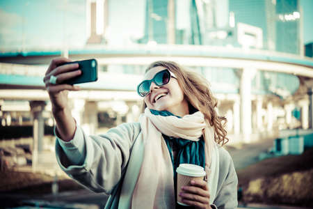 Young beautiful woman takes a selfie with Moscow City international business center in the background. Toned pictureの写真素材