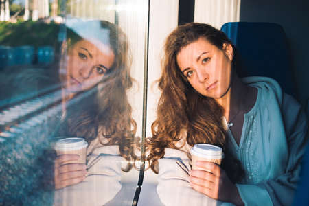 Young beautiful woman enjoys her coffee during the train ride.