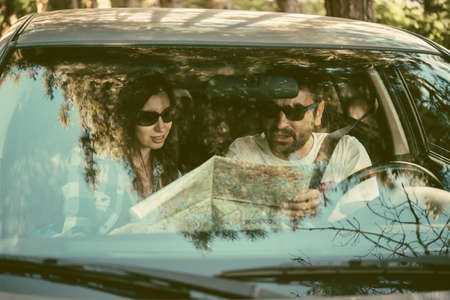 Young man and woman hold road map in a car. Travel and adventure concept. Toned pictureの写真素材