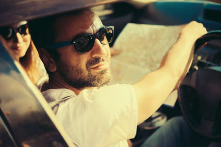 Young beautiful man holds a road map in a car. Travel and adventure concept. Toned pictureの写真素材