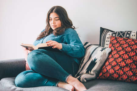 Beautiful woman sitting on sofa reading a book. Toned pictureの写真素材