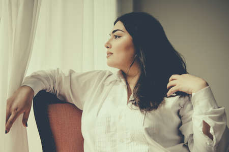 Portrait of beautiful plus size girl in white sitting in the armchair. Toned pictureの写真素材