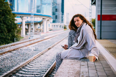 Young beautiful woman sits on the platform while waiting for the train.の写真素材