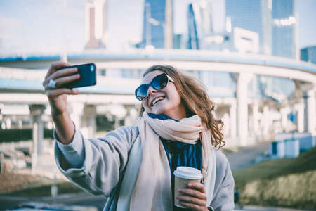 Young beautiful woman takes a selfie with Moscow City international business center in the background.の写真素材