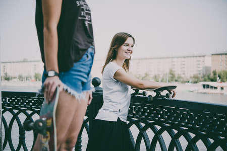 Two young girls enjoy skateboarding in the park in summer. Active live and sport concept. Toned pictureの写真素材