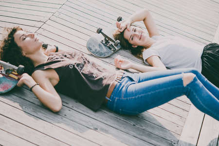Two young girls enjoy skateboarding in the park in summer. Active live and sport concept. Toned pictureの写真素材