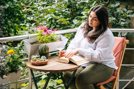 Portrait of beautiful plus size girl reading a book on balcony or terrace of cafeの写真素材
