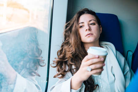 Young beautiful woman enjoys her coffee during the train ride.