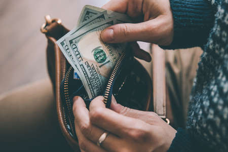Girl's hands holding dollar bills, small money pouch and leather bag. Toned picture