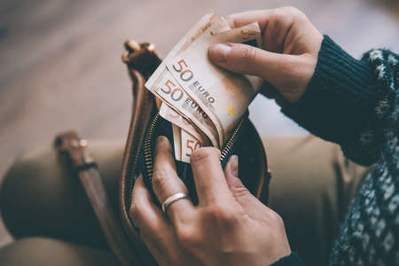Girl's hands holding dollar bills, small money pouch and leather bag. Toned pictureの写真素材