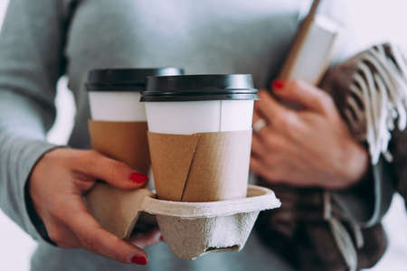 Take-away coffee seen in hands with a book and blanket in the background. Picnic and going out concept.の写真素材