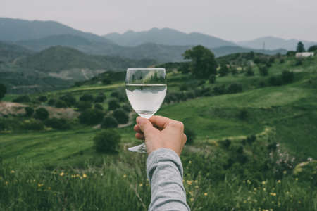 Hand holding a glass of white wine with mountains in the background. Toned pictureの写真素材