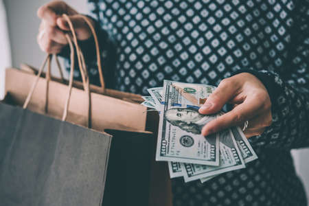 Hands holding dollar bills and paper bags. Shopping concept. Toned pictureの写真素材