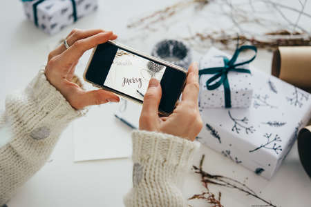 Girl making photo of gift boxes with her smartphone. Christmas or New year gift packing. Holiday decor concept.の写真素材