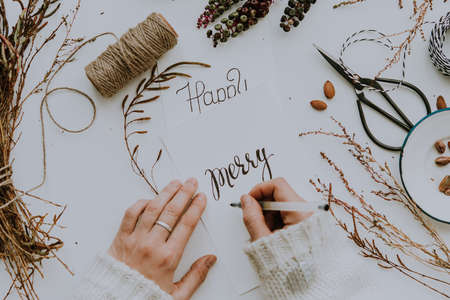 Female hands writing on a handmade postcard. Christmas or New year holiday decor concept. Top view. Toned pictureの写真素材