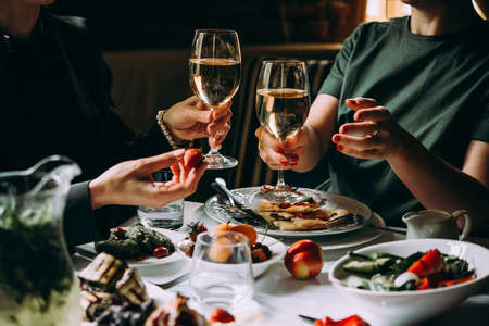Dinner with friends of family served in a restaurant. Two glasses of white wine in handsの写真素材