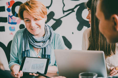 Young woman giving a presentation with tablet in creative office. Successful feminine teamwork and business brainstorming concept. Toned imageの写真素材
