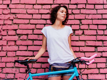 Young beautiful girl stands with her single speed of fixed gear bicycle with a bright wall in the background.の写真素材