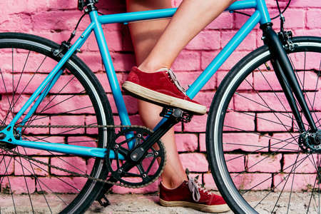 Young beautiful girl's legs and single speed of fixed gear bicycle with a bright wall in the background.の写真素材