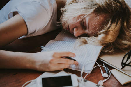 A tired teenage girl sleeping on her table while doing her school homework. Laziness and procrastination concept. Toned imageの写真素材