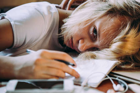 A tired teenage girl sleeping on her table while doing her school homework. Laziness and procrastination concept