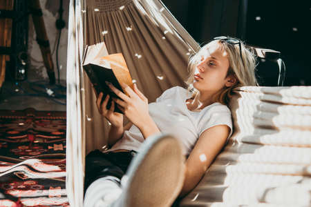 A teenage girl is reading book in a hammockの写真素材