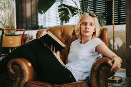 A teenage girl is reading book in an armchairの写真素材