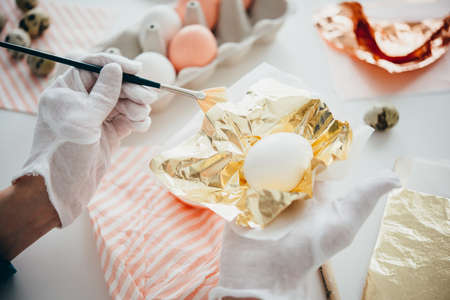 Hands coating an egg with golden foil. Modern style easter eggs painting.の写真素材
