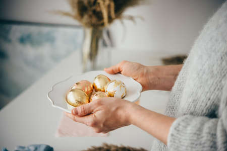 Hands holding a plate with modern style golden foil coated easter eggs.の写真素材