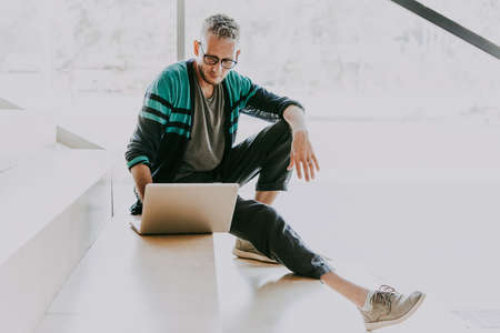 Mature handsome man sitting at the steps working on his laptop.の写真素材