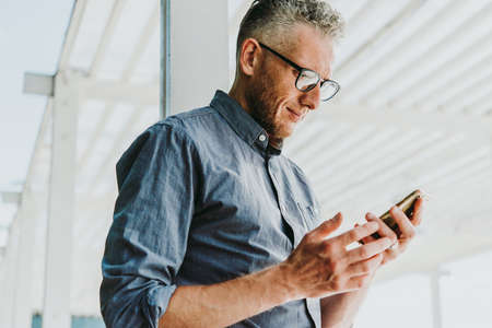 Mature handsome man relaxing outside and using his smarthponeの写真素材